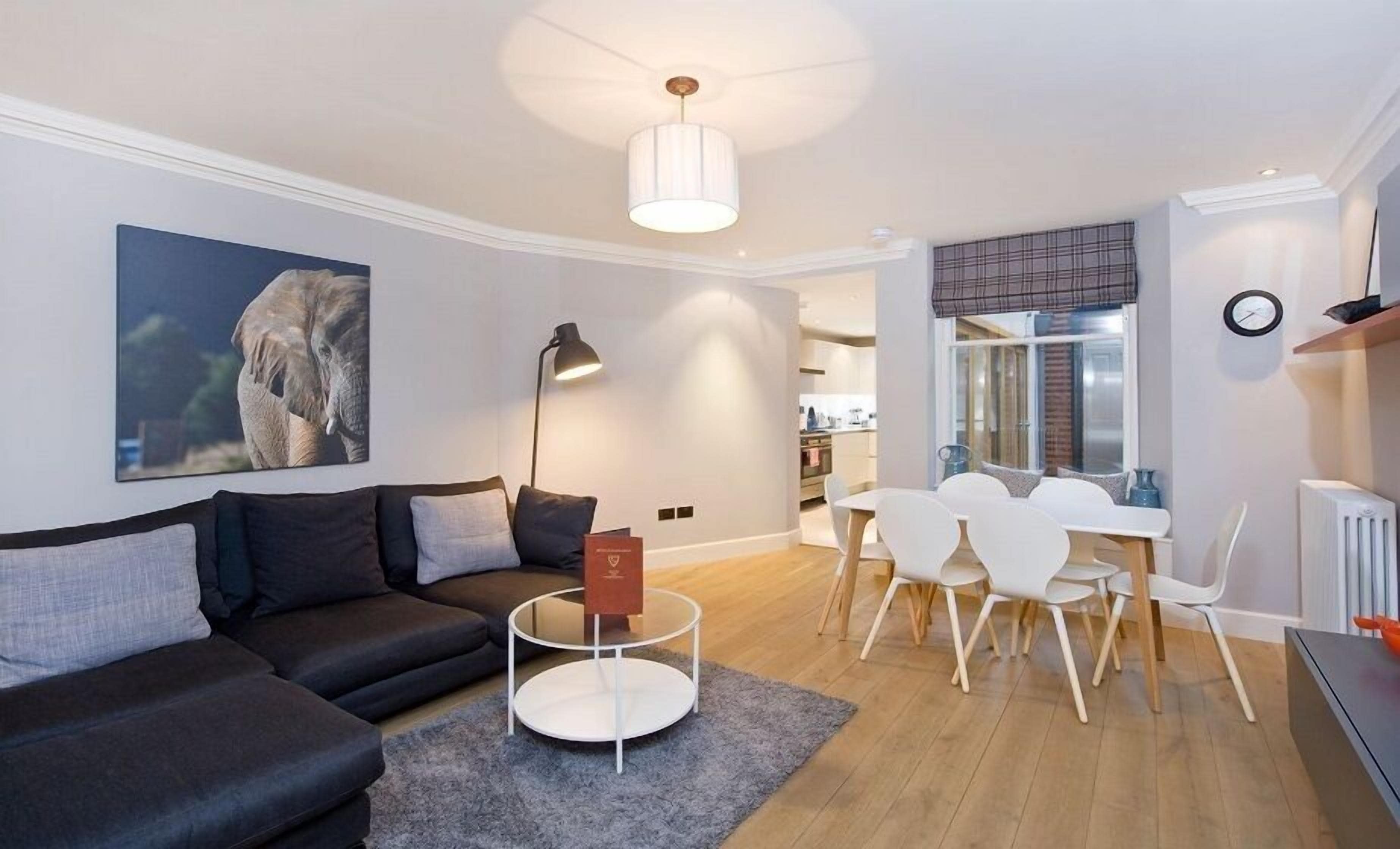 Ein modernes Wohnzimmer mit einem dunklen Sofa, einem runden Couchtisch und einem Essbereich mit weißen Stühlen und einem Tisch.