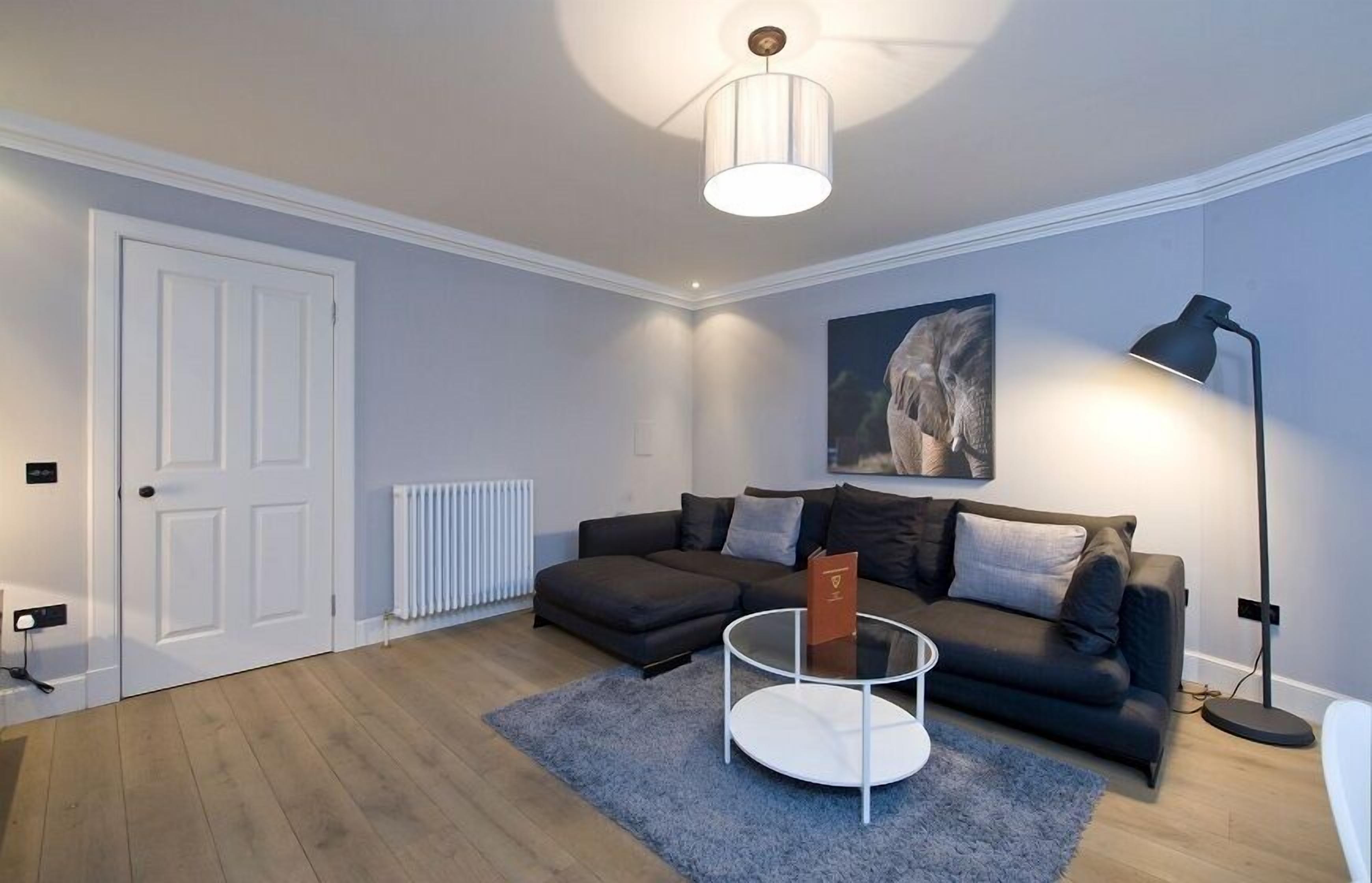 A modern living room with a dark sofa, a round coffee table, a lamp, and a framed picture on the wall.