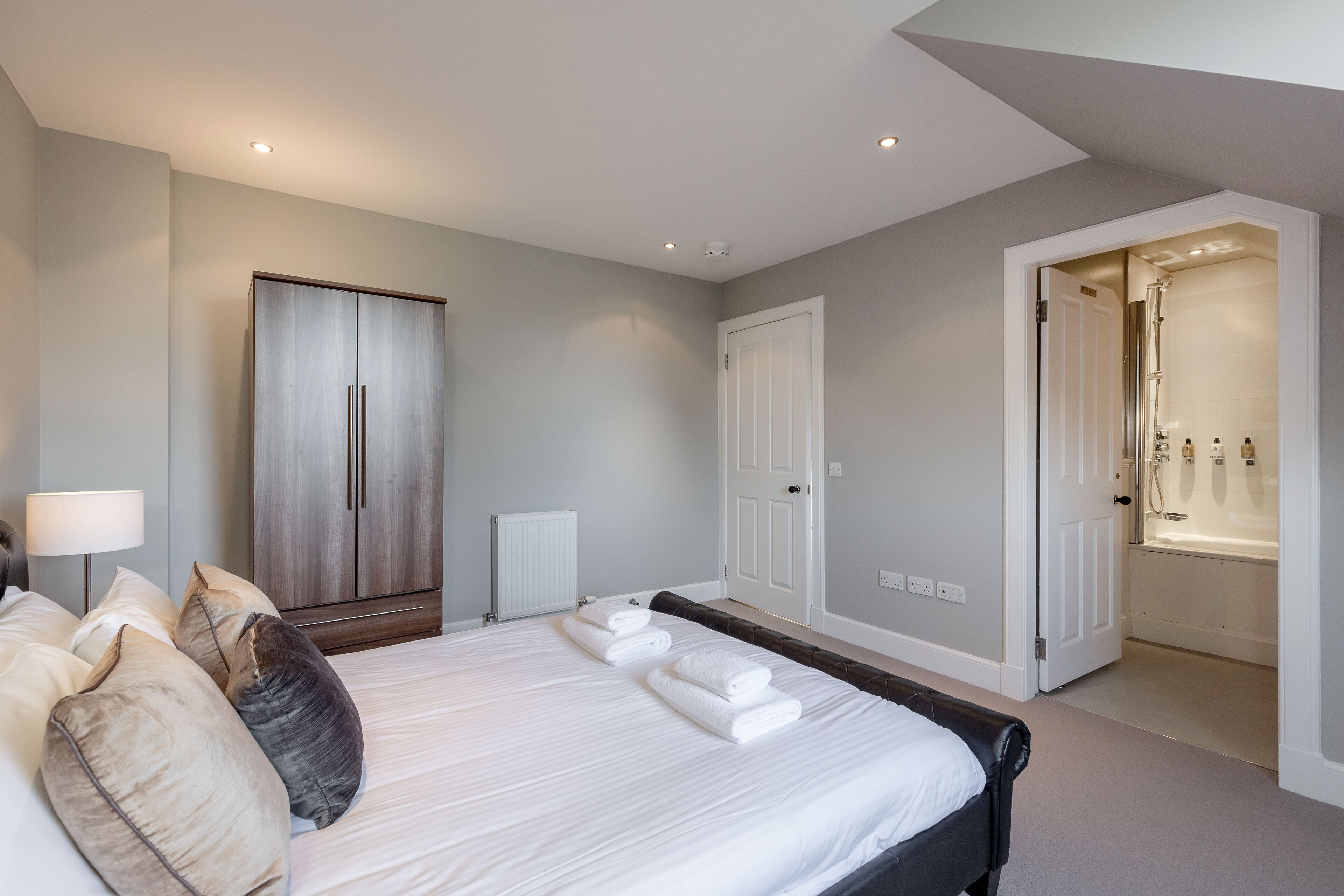 A bedroom with a large bed, a wardrobe, a radiator, and a bathroom with a bathtub and shower.