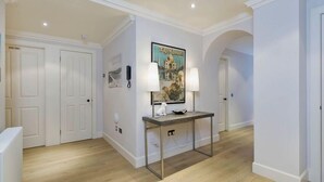 A hallway with white walls, a wooden floor, a framed picture of Taj Mahal, and a small table with two lamps. - Destiny Scotland - Q-Residence (Edinburgh)