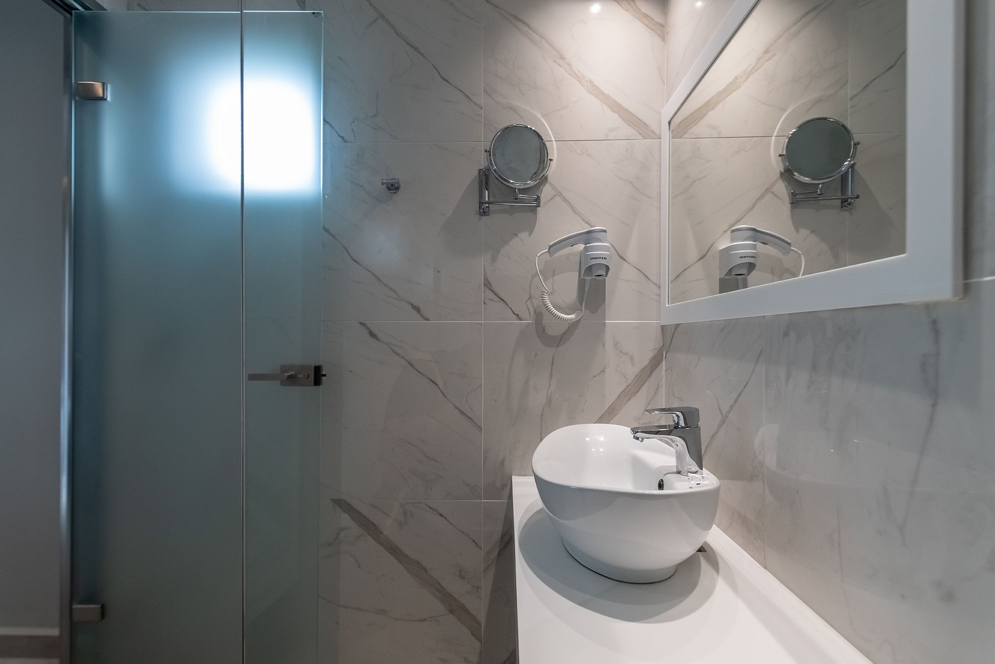 A modern bathroom with a white sink, a mirror, and a handheld showerhead.