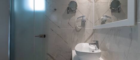 A modern bathroom with a white sink, a mirror, and a handheld showerhead.