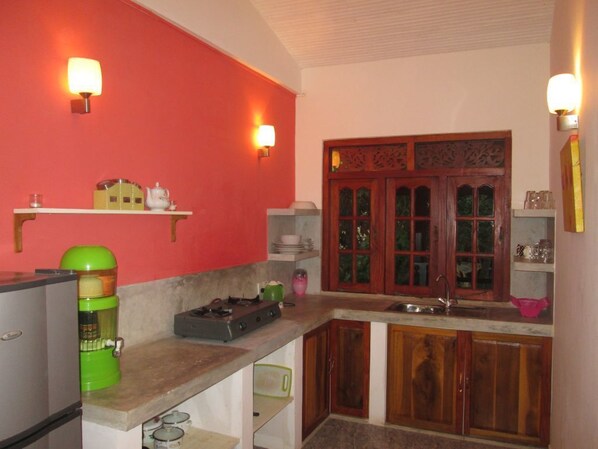 A kitchen with a red wall, wooden cabinets, a green coffee maker, and a stove.