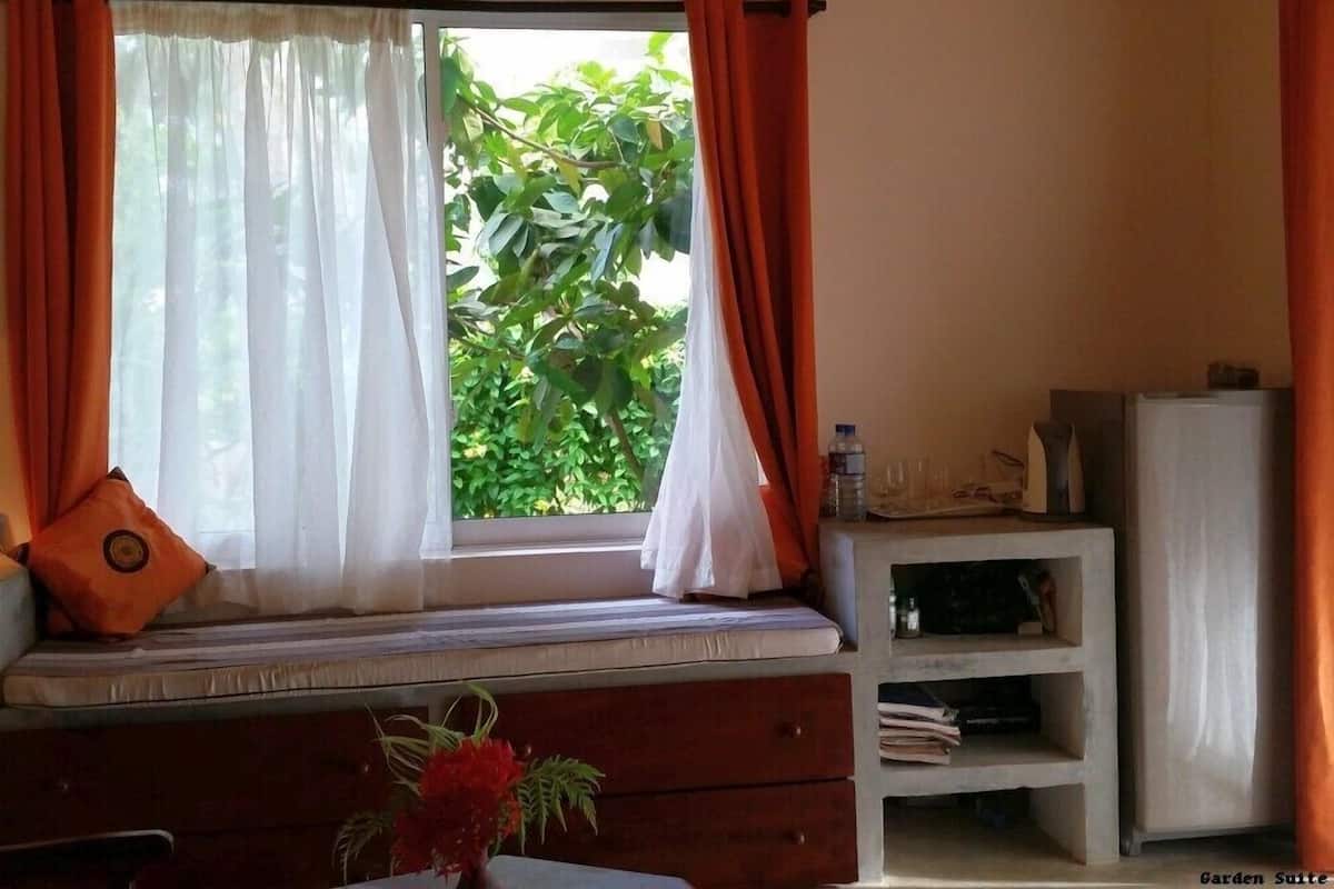 Una habitación con un asiento junto a la ventana, una pequeña mesa con un florero y un mueble blanco.