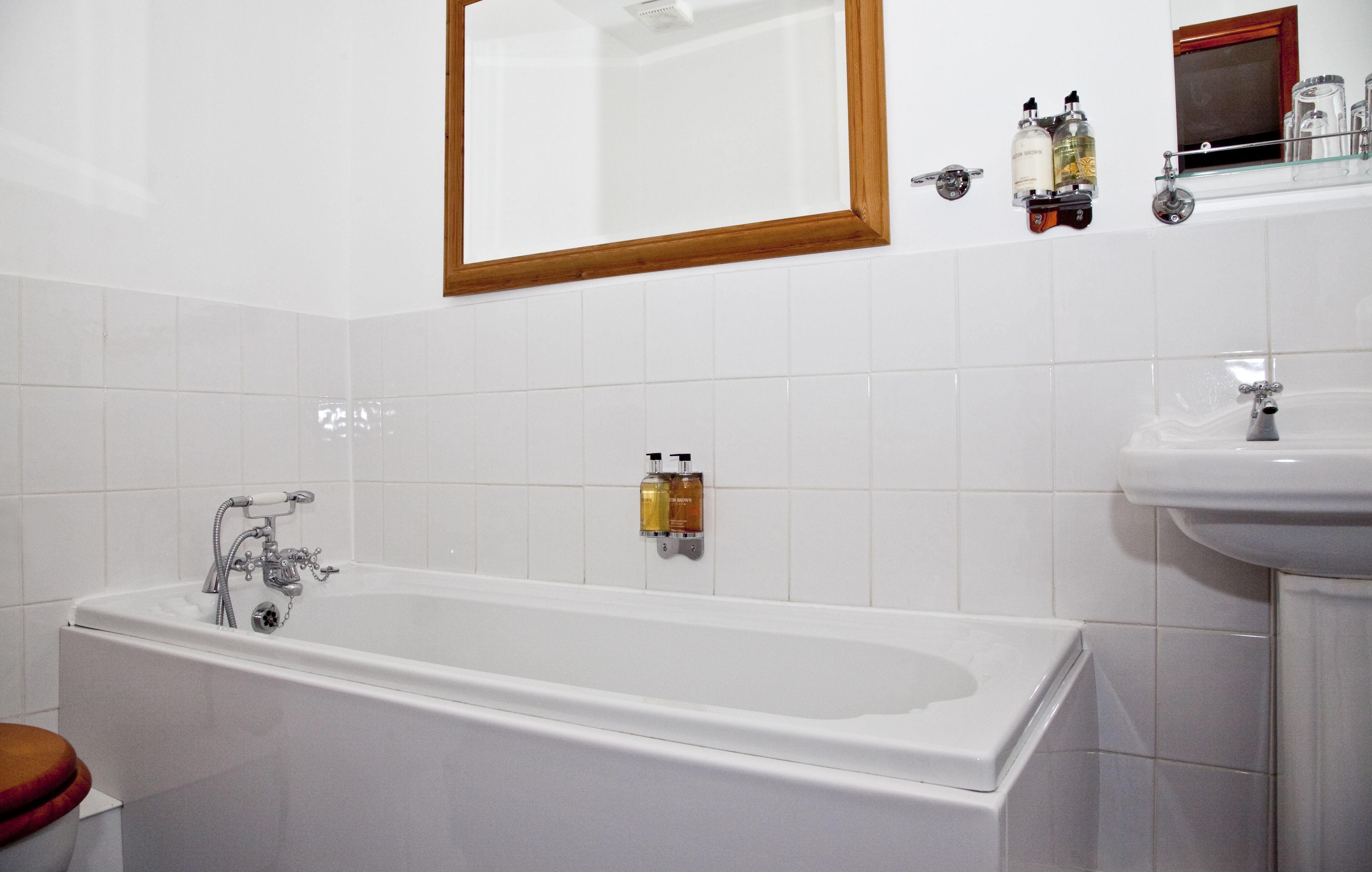 A bathroom with a bathtub, a sink, and a mirror. There are toiletries on the wall.