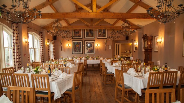 Un espace repas avec des tables et des chaises en bois, des lustres et des œuvres d’art encadrées accrochées aux murs.