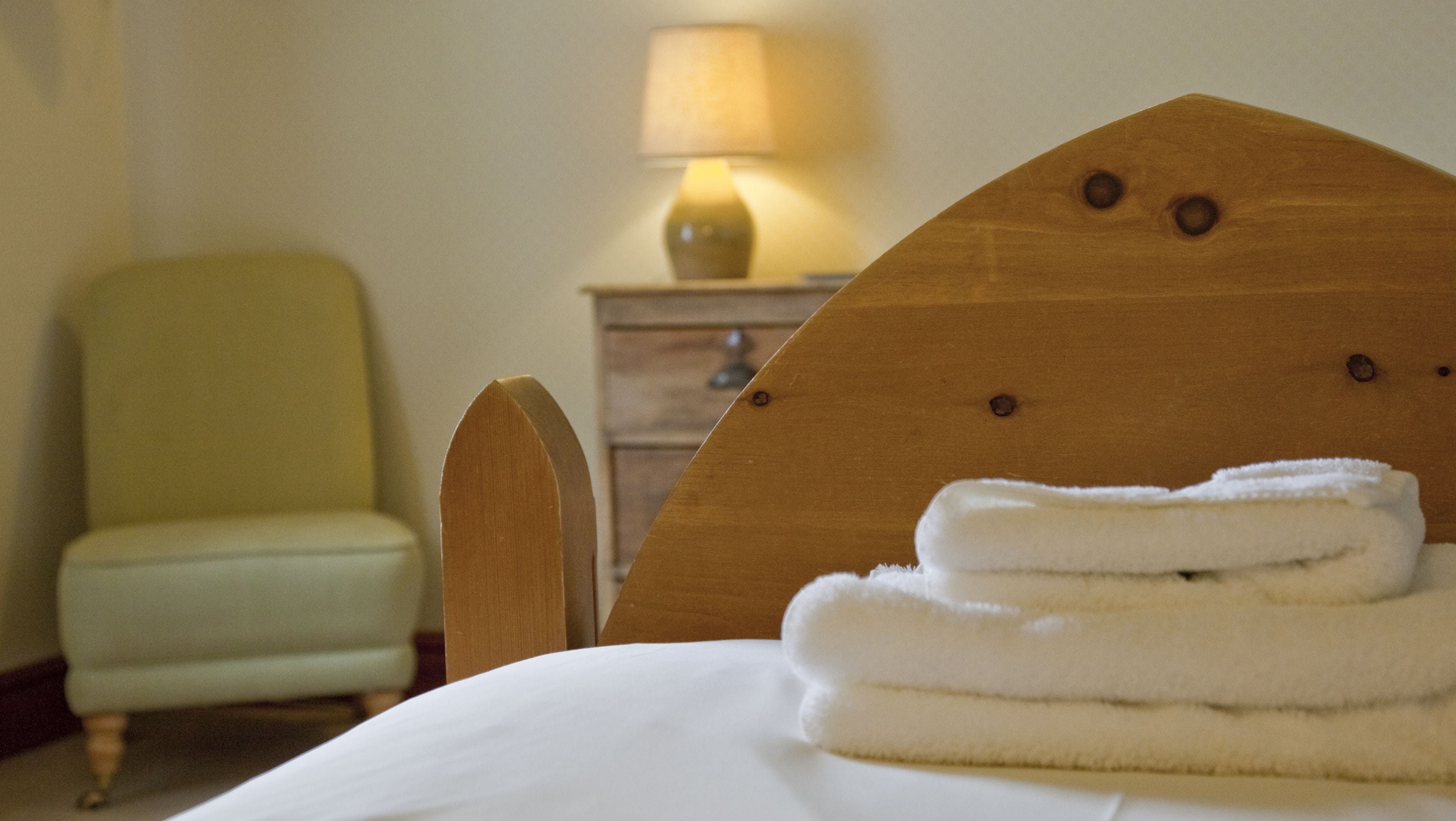 Een hotelkamer met een bed, een houten hoofdbord, een lamp en een stoel.