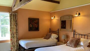 A bedroom with two single beds, a window with floral curtains, a painting on the wall, and a mirror above the bed.