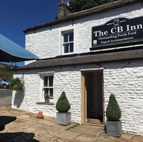 A white building with a sign that reads 'The CB Inn' and mentions 'Outstanding Fresh Food' and 'Superb Accommodation.'