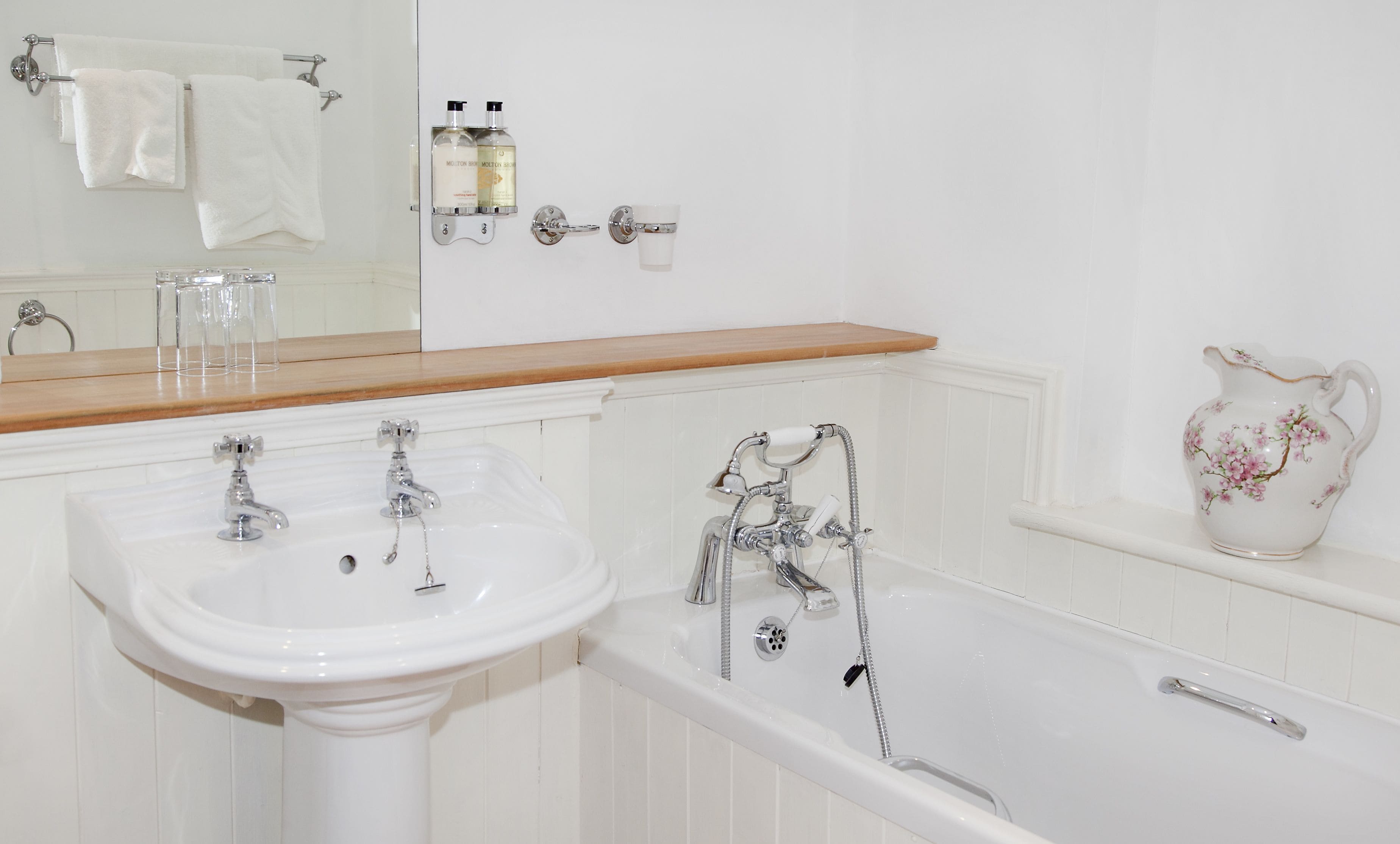 A bathroom with a white sink, a bathtub, and a mirror above the sink.