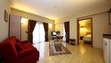 Habitación de hotel con sofá rojo, zona de comedor con mesa y sillas, televisor y cama.