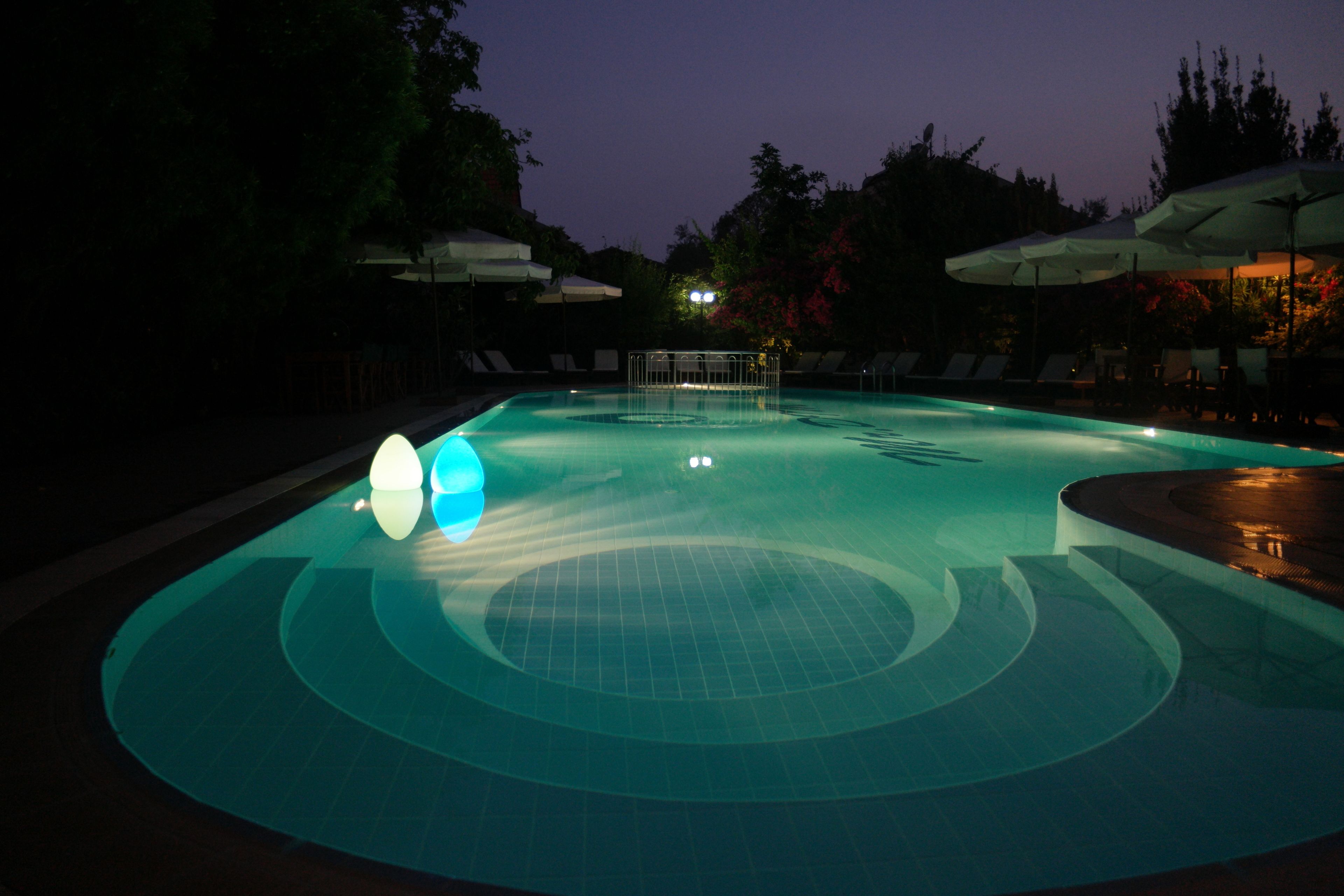 An outdoor swimming pool at dusk with lounge chairs and umbrellas.