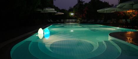 An outdoor swimming pool at dusk with lounge chairs and umbrellas.