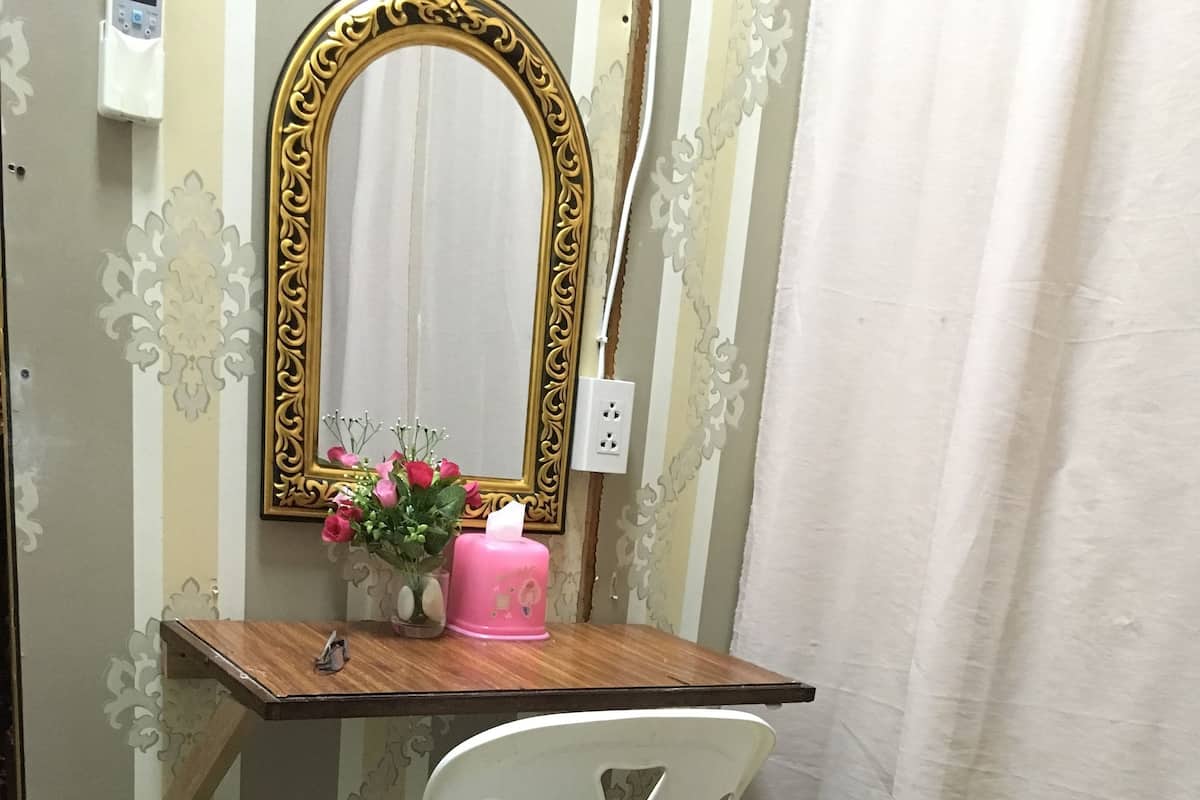 A bathroom with a wooden vanity, a white plastic chair, a green trash bin, a pink candle, and a mirror with an ornate frame.