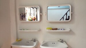 A bathroom with two sinks, a mirror, and a shelf with toiletries.