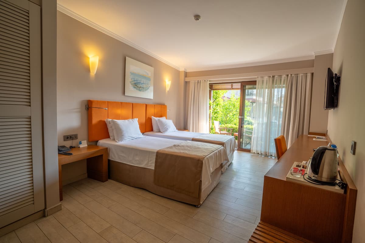 Une chambre d’hôtel avec deux lits, un bureau, une machine à café et une vue sur la verdure.