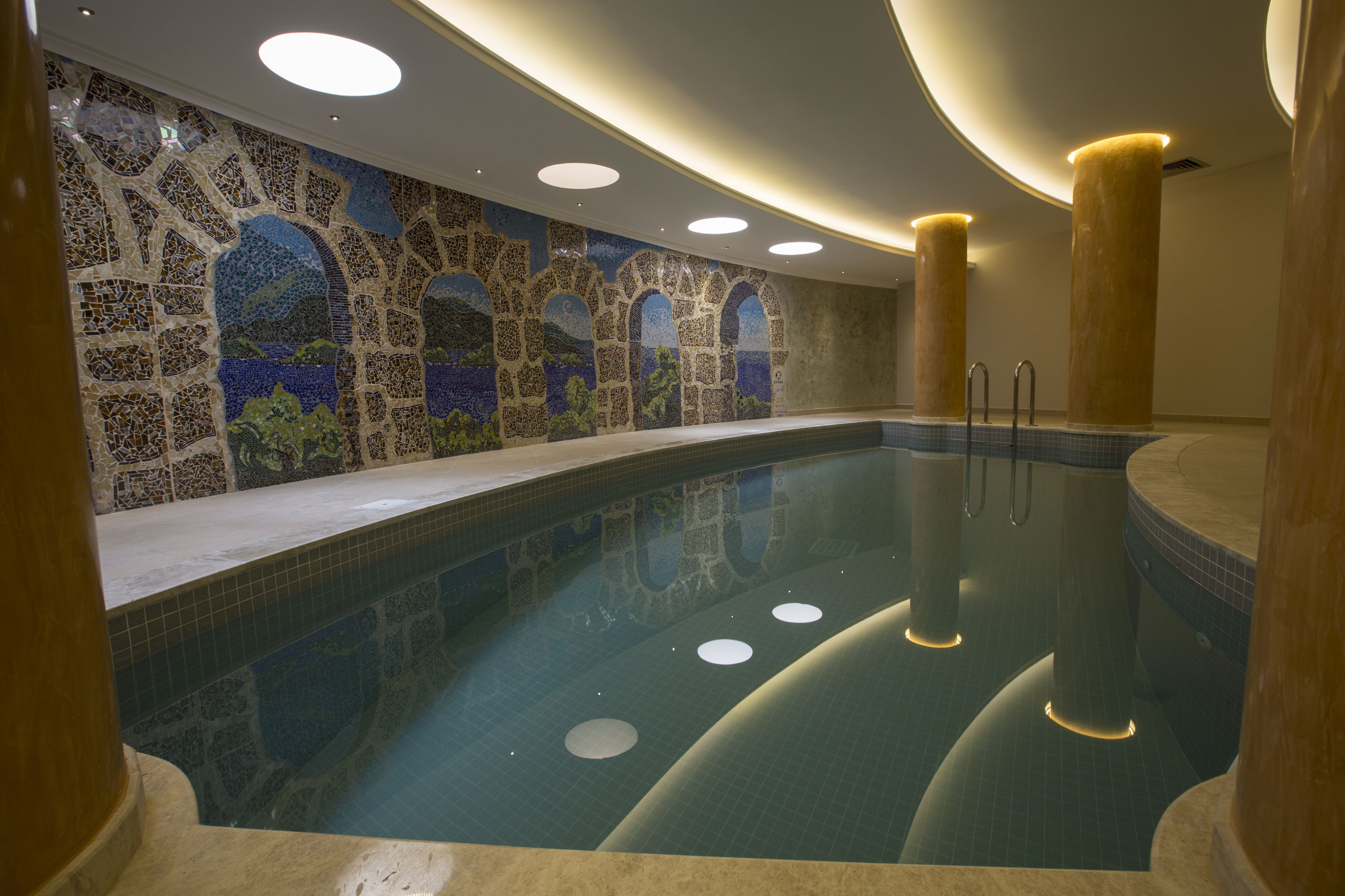 A large indoor swimming pool with mosaic tile walls and multiple lights.
