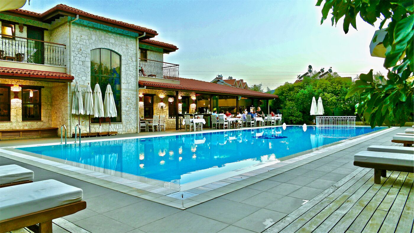 A pool area with lounge chairs, a restaurant with outdoor seating, and a stone building with a balcony.