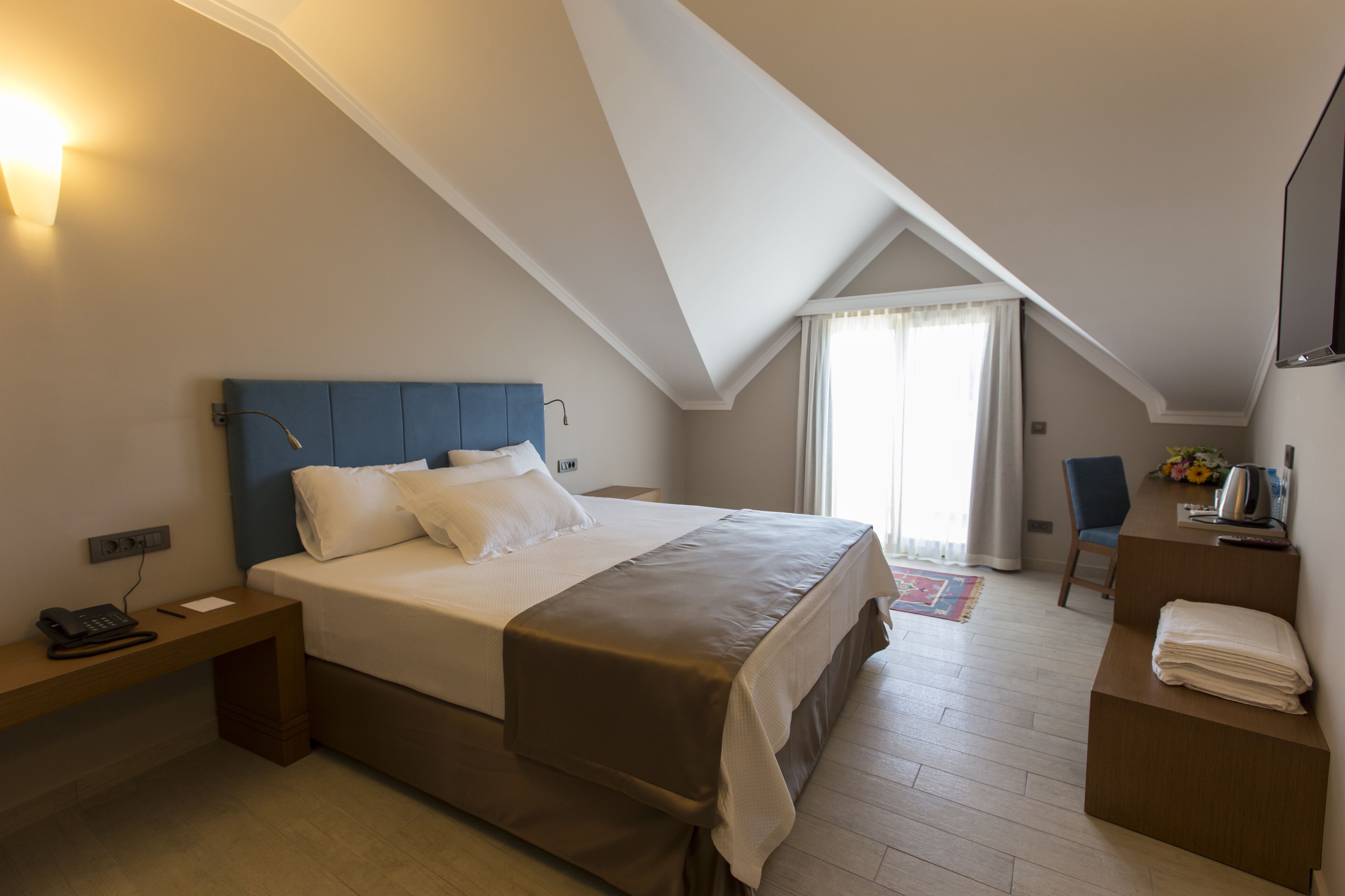 Una habitación de hotel con una cama grande, un escritorio, una silla y una mesita con un florero.