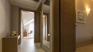 Un couloir avec une porte en bois, un petit bureau sur lequel est posé un vase de fleurs et un tableau encadré accroché au mur.