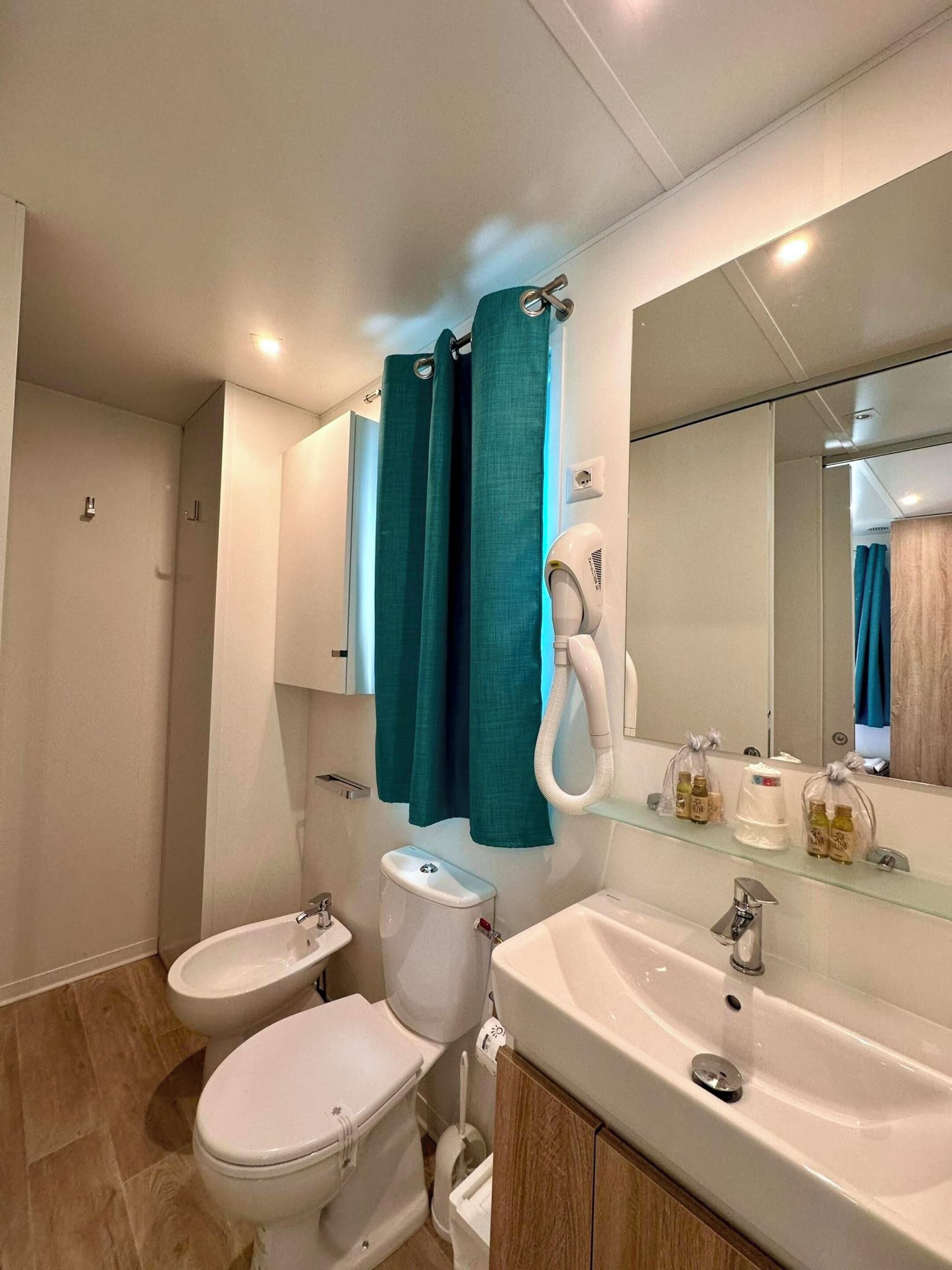 Une salle de bain équipée de toilettes, d’un bidet, d’un lavabo et d’un miroir.