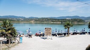 Une plage avec des parasols et des palmiers, un panneau indicateur, et une vue sur des montagnes en arrière-plan.