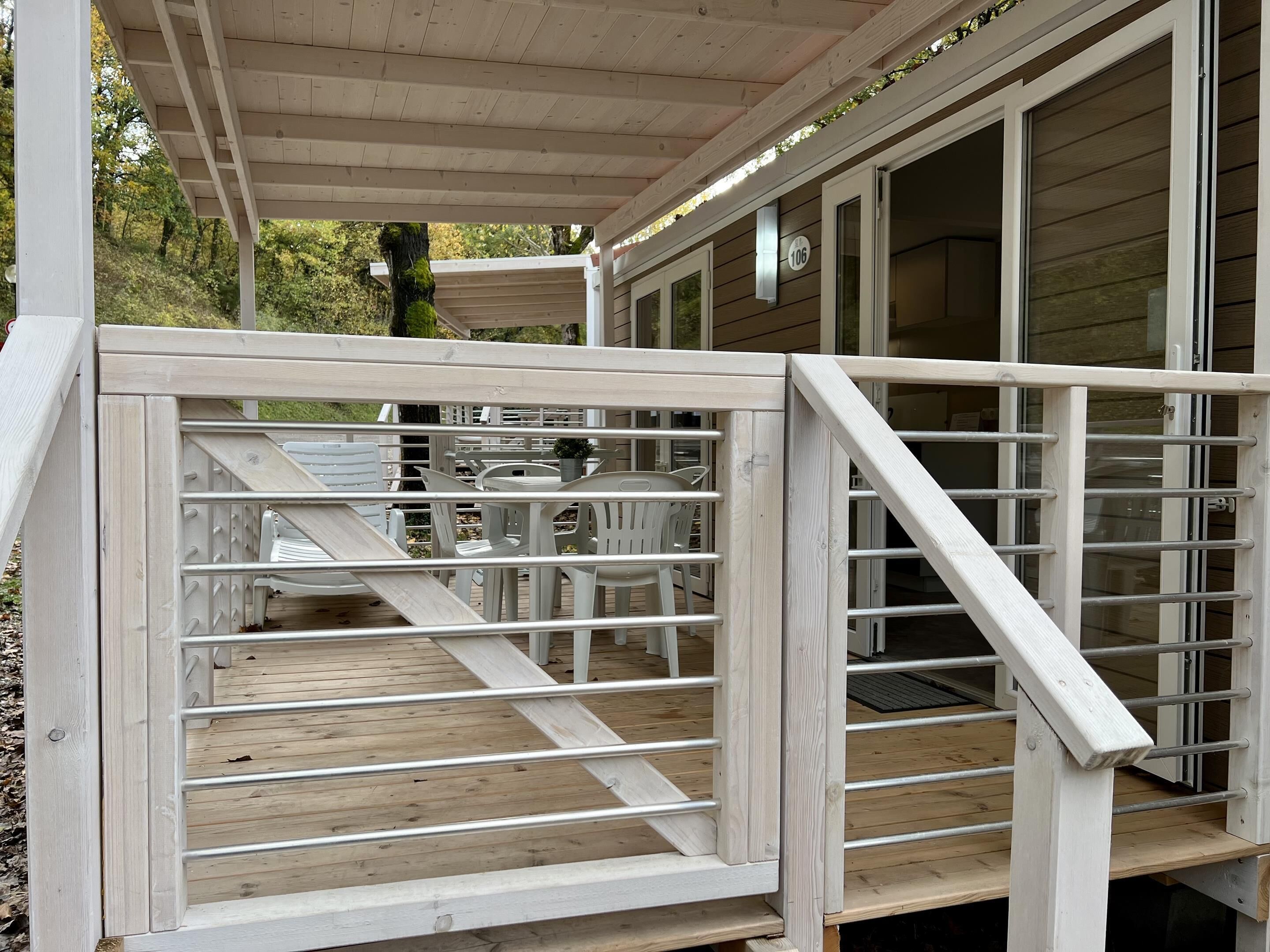 Eine Holzterrasse mit Metallgeländer, Sitzgelegenheiten im Freien und einem überdachten Bereich.