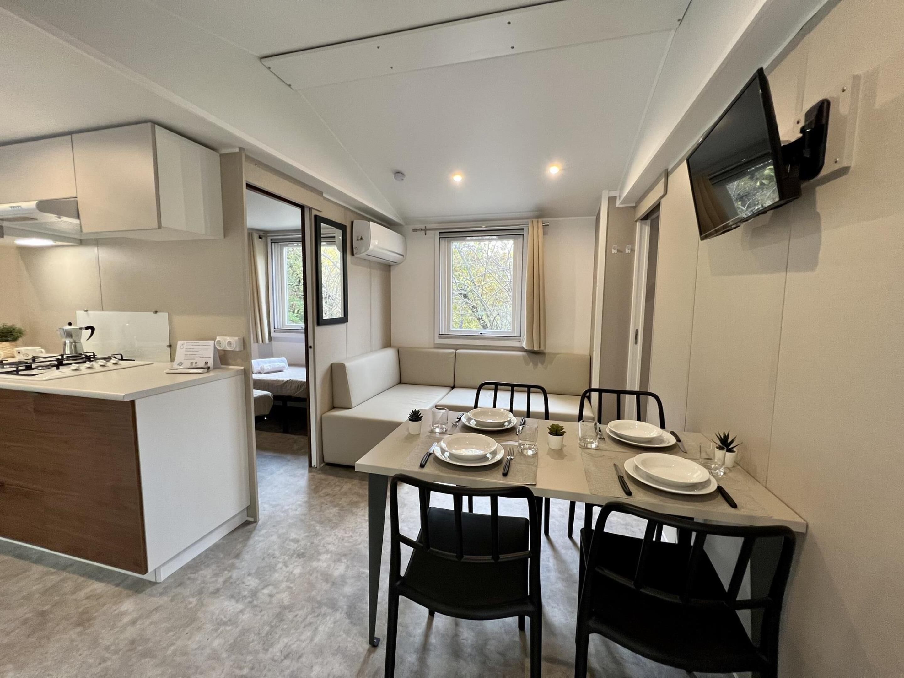 A compact kitchen with a dining area, a built-in bench, and a TV mounted on the wall.
