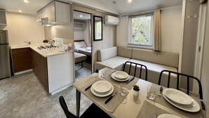 Une cuisine compacte équipée d’une cuisinière, d’un évier et de placards, un coin repas avec une table pour quatre personnes, et un espace salon confortable avec une fenêtre donnant sur la verdure.