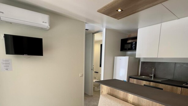 A modern kitchen with a built-in oven, a microwave, and a sink. There is a beige sofa and a flat-screen TV mounted on the wall.