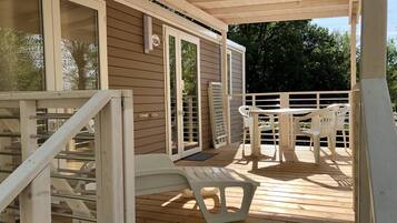 Een houten terras met een overdekte ruimte, witte plastic stoelen en een tafel.