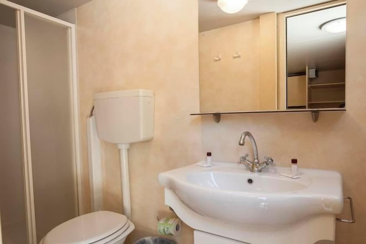 A bathroom with a white toilet, a white sink with a mirror above it, and a beige wall.