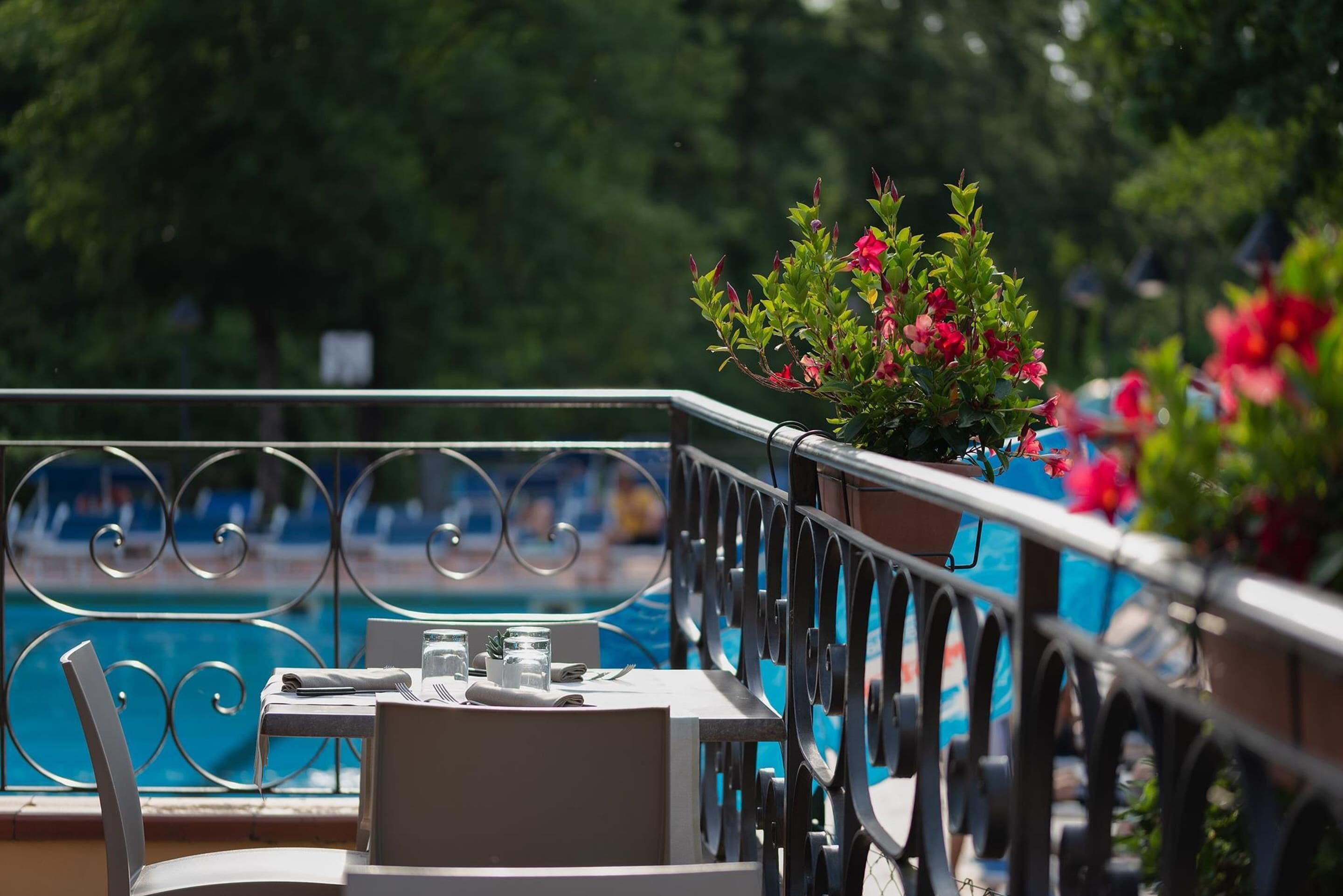 A balcony with a table and chairs, overlooking a swimming pool.