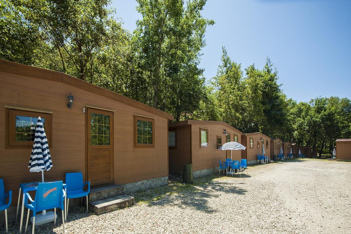 Filera de cabanes de fusta amb caires blaus i ombrel·les estriades, situades sobre un camí de grava amb arbres al fons.