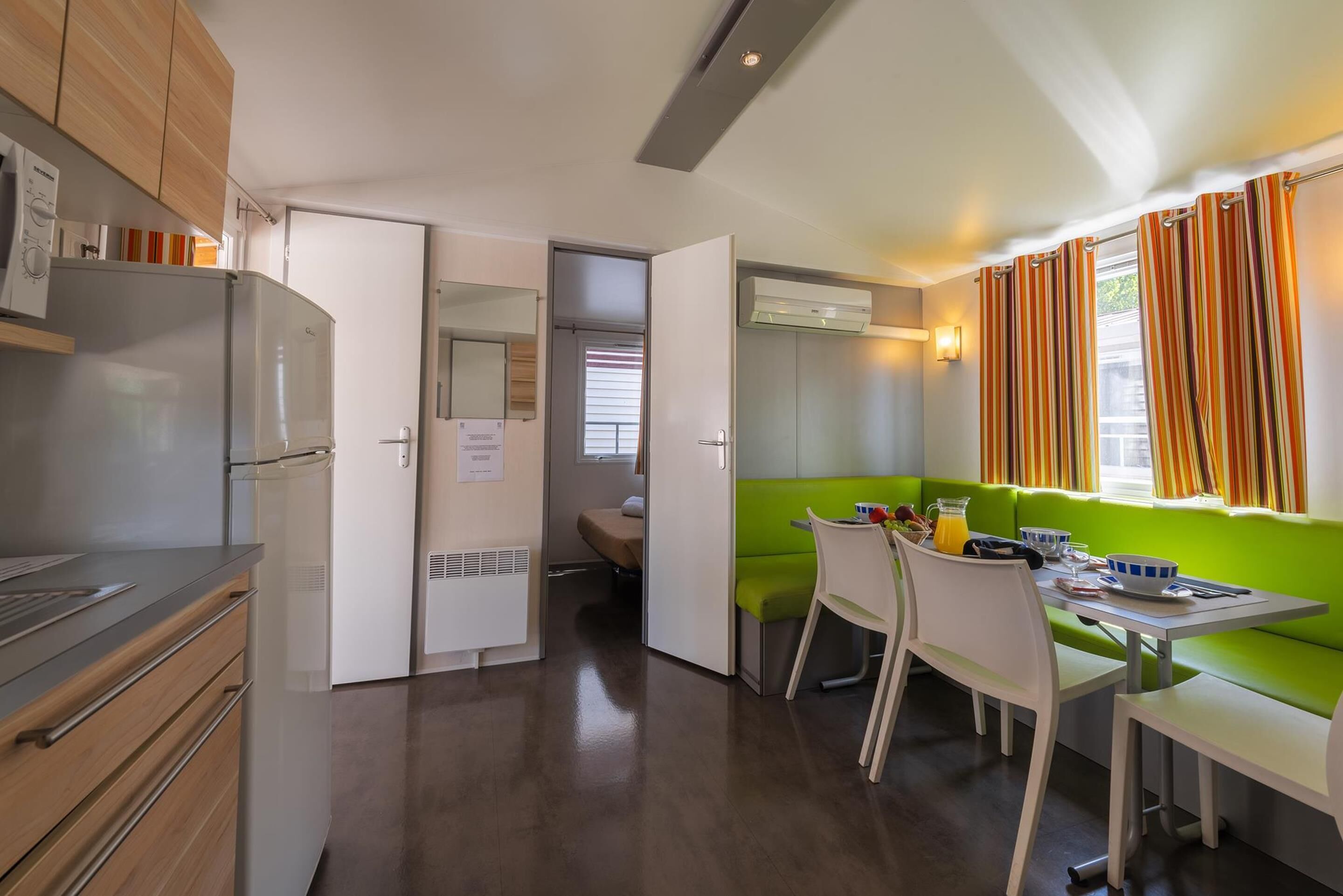 A modern kitchen with a dining area, wooden cabinets, a built-in oven, and a green cushioned bench.