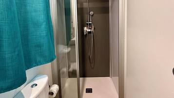 Et lille badeværelse med toilet, en brusekabine med glasvægge og en bruseforhæng i turkis.