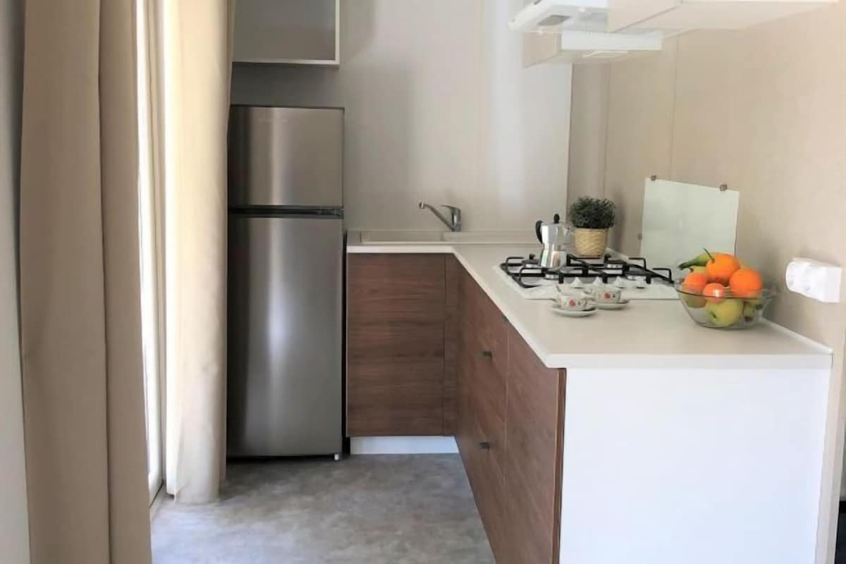 A compact kitchen with a stainless steel refrigerator, a gas stove, and a small countertop with a bowl of fruit.