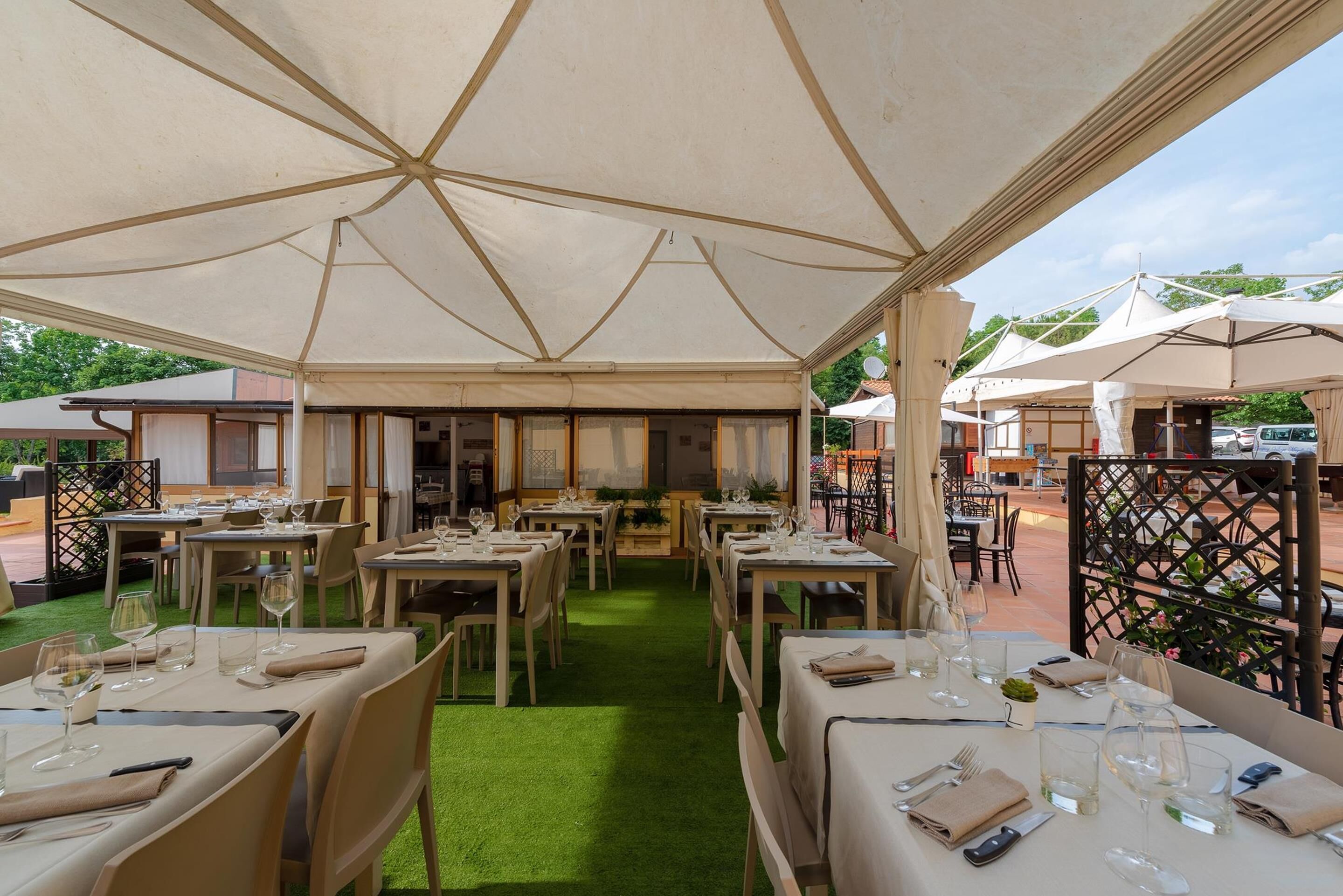 Un área de comedor al aire libre con mesas dispuestas para dos personas, cubierta por un toldo grande.