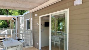 Un espace extérieur abrité, doté d’une terrasse en bois, de chaises en plastique blanc et d’une table.