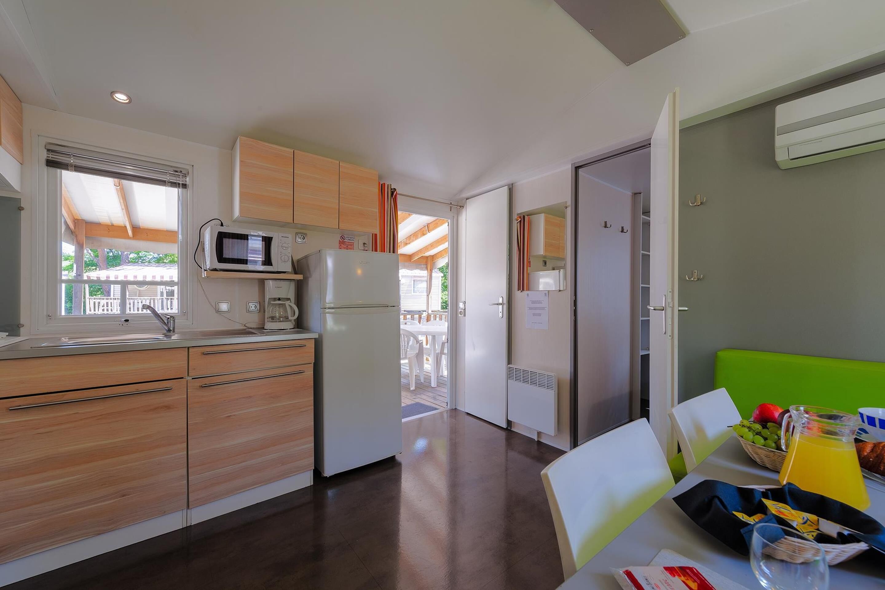 A compact kitchen with a microwave, refrigerator, and wooden cabinets. A dining area with a table and chairs is visible, along with a breakfast setup including fruits and a jug of juice.