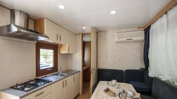 Una cocina compacta con estufa a gas, lavamanos y alacenas, que da a un comedor con una mesa para dos personas y un sofá.