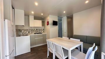 A compact kitchen with white cabinets, a tiled backsplash, and a built-in stove. There is a dining table with white chairs and a grey sofa.
