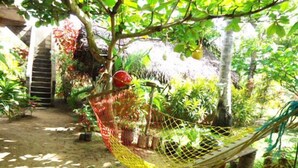A hammock hanging from a tree in a garden with various plants and a wooden structure in the background. - Natural Cabanas (Tangalle)