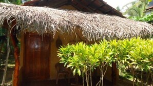 A small, thatched-roof hut with a wooden door and a single chair outside. - Natural Cabanas (Tangalle)