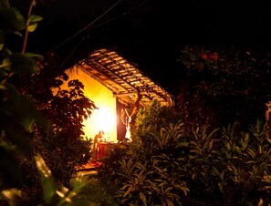 A small, illuminated structure surrounded by dense foliage at night. - Natural Cabanas (Tangalle)