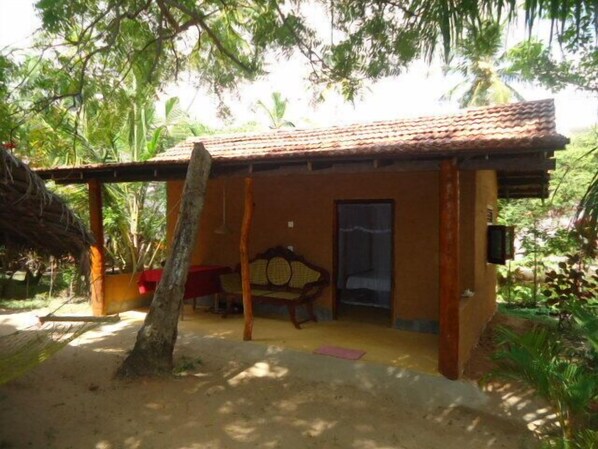 A small, single-story building with a tiled roof, a porch with a wooden bench, and a door. - Natural Cabanas (Tangalle)
