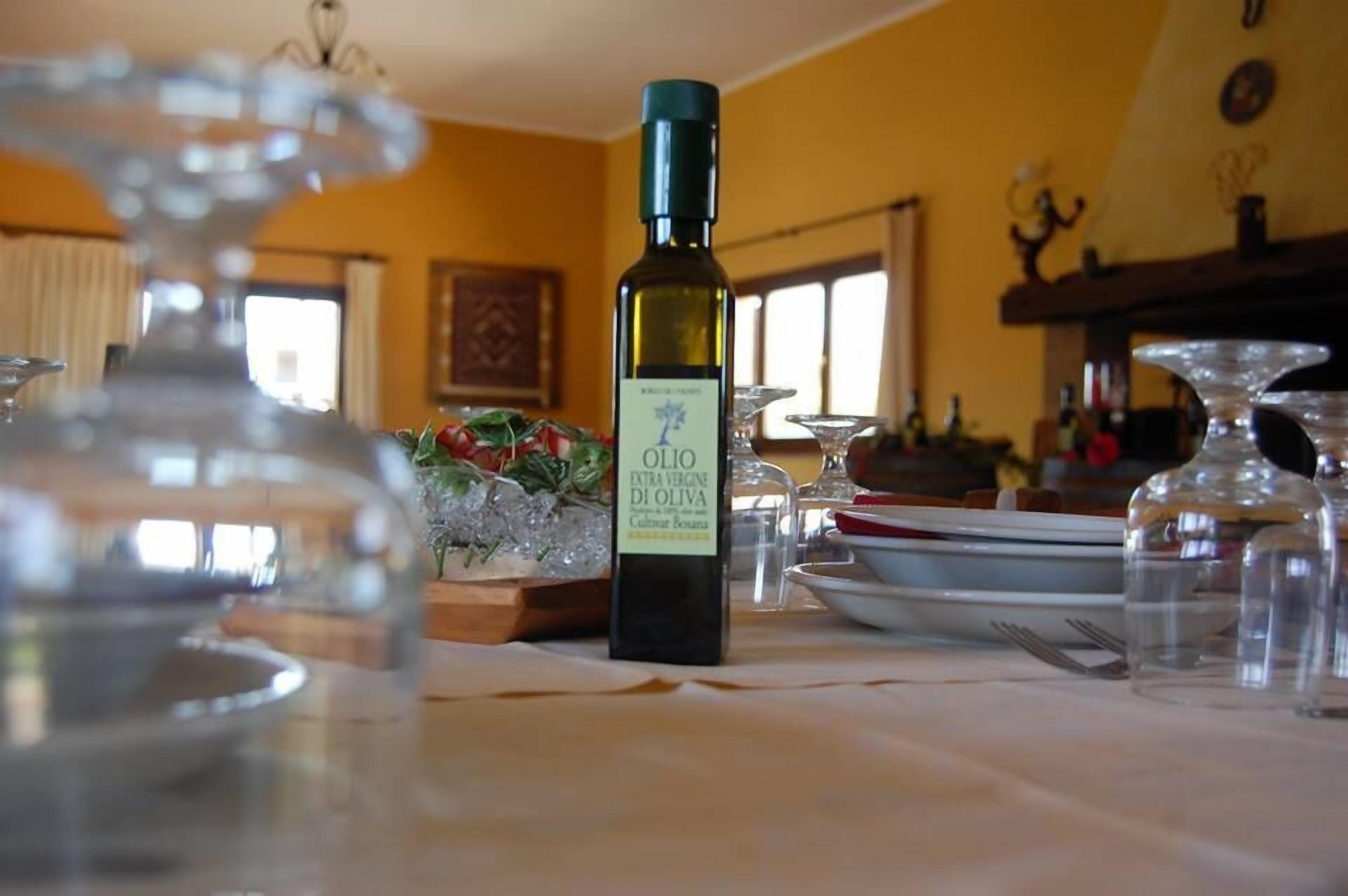 Eine Olivenölflasche auf einem Tisch zusammen mit Gläsern und einer Schüssel mit Grünzeug.