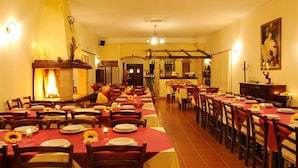 Un restaurant avec de nombreuses tables dressées pour le service, décorées de nappes rouges et jaunes et agrémentées de bougies.