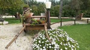 Un décor extérieur rustique, avec un chariot en bois rempli de plantes en pot et de fleurs, entouré d’un chemin de gravier et d’une clôture en bois.