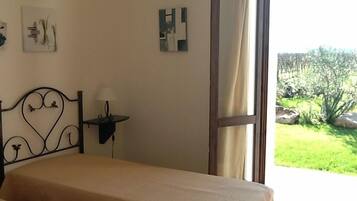 A bedroom with a bed, a bedside table with a lamp, a window with a view of a garden, and wall art.